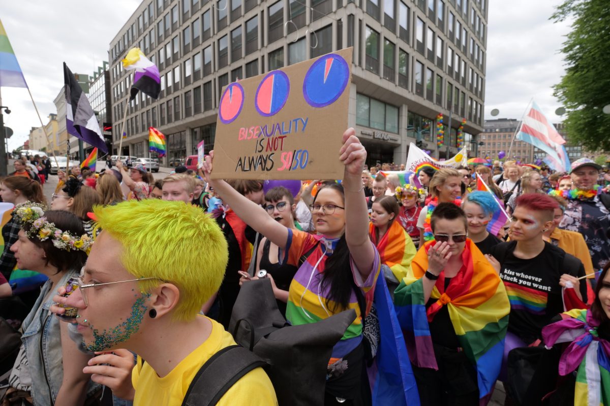 Väkijoukko ja kyltti jossa lukee "bisexuality is not always 50/50"