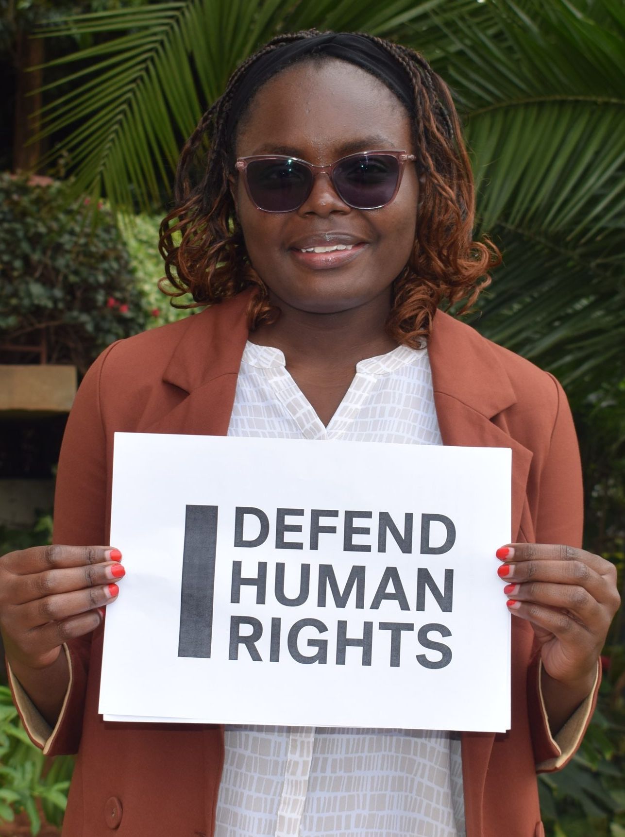 Michelle Mwelesa's brave action. They are looking into the camera smiling and holding a sign that says "I Defend Human Rights."