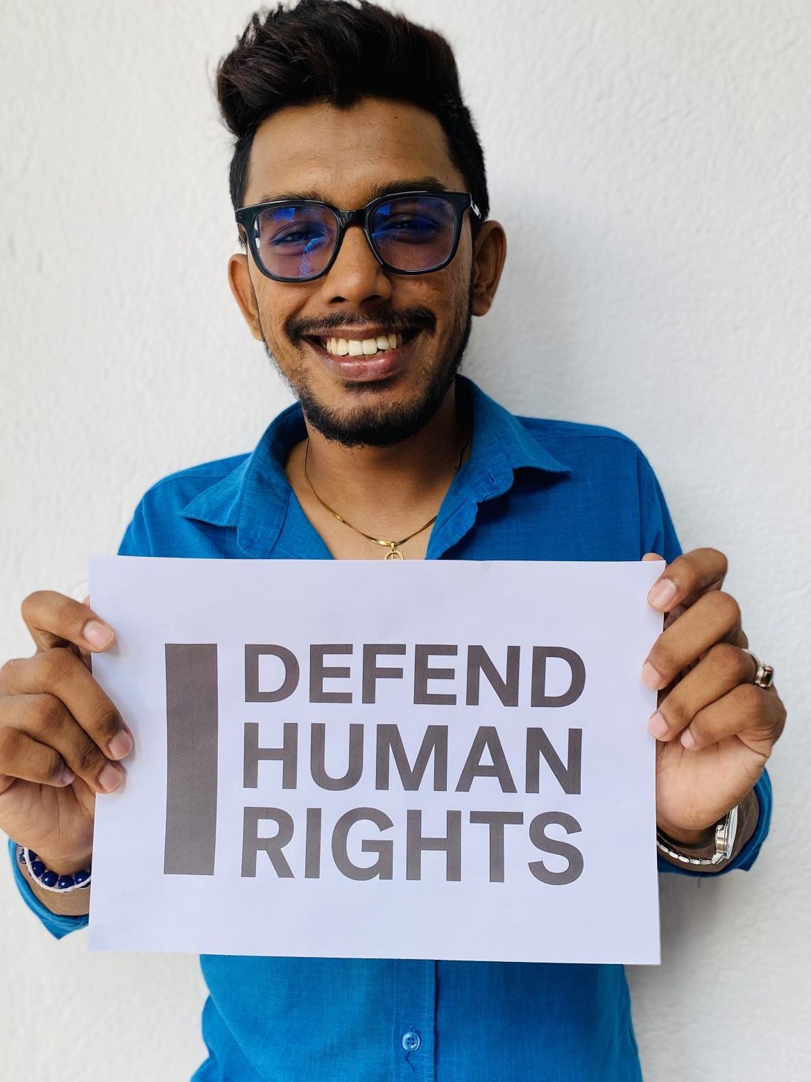 Akash Abhisheks' brave action. They are looking into the camera smiling and holding a sign that says "I Defend Human Rights."
