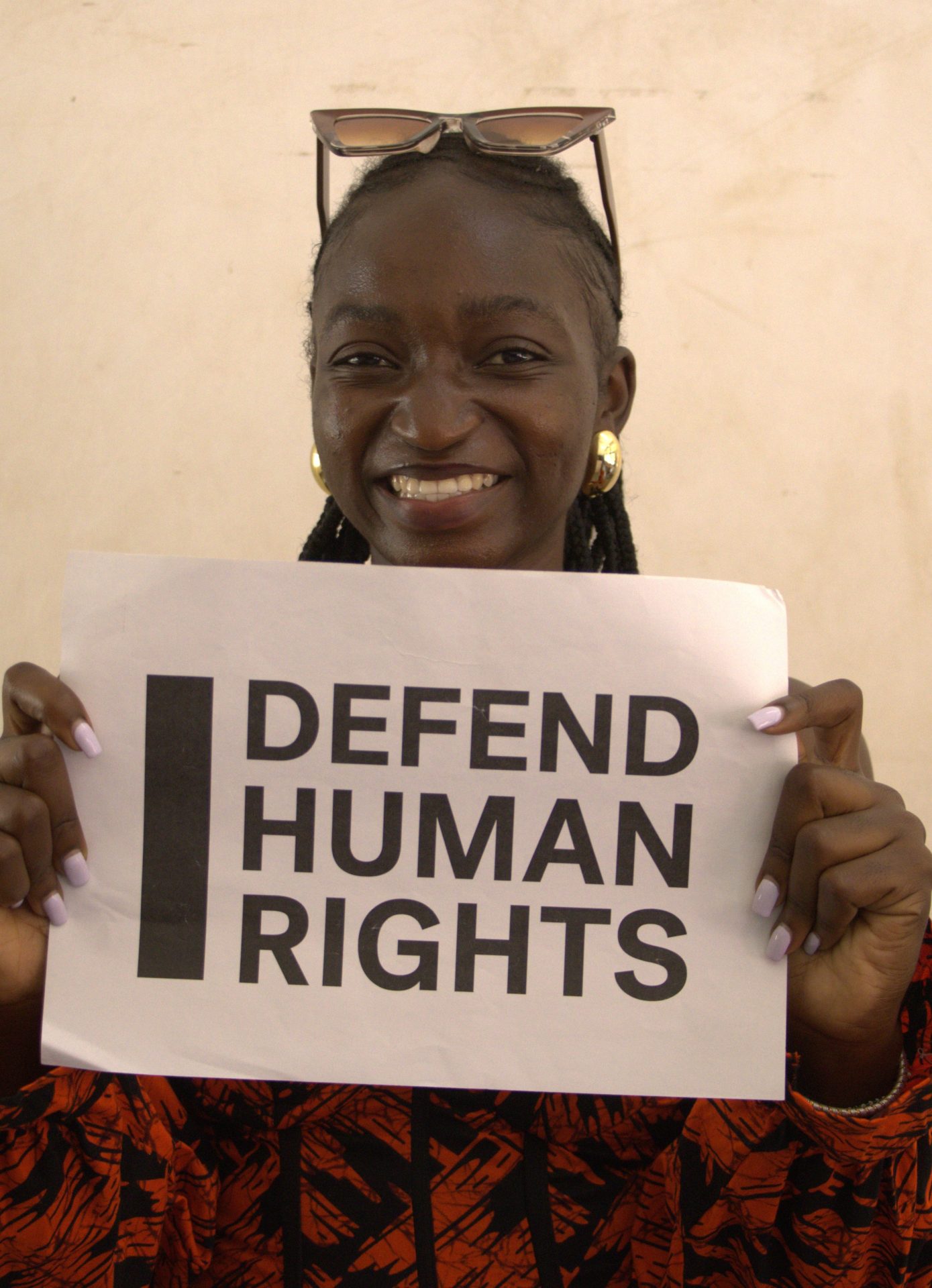 Grace Adonai's brave action. They are looking into the camera smiling and holding a sign that says "I Defend Human Rights."
