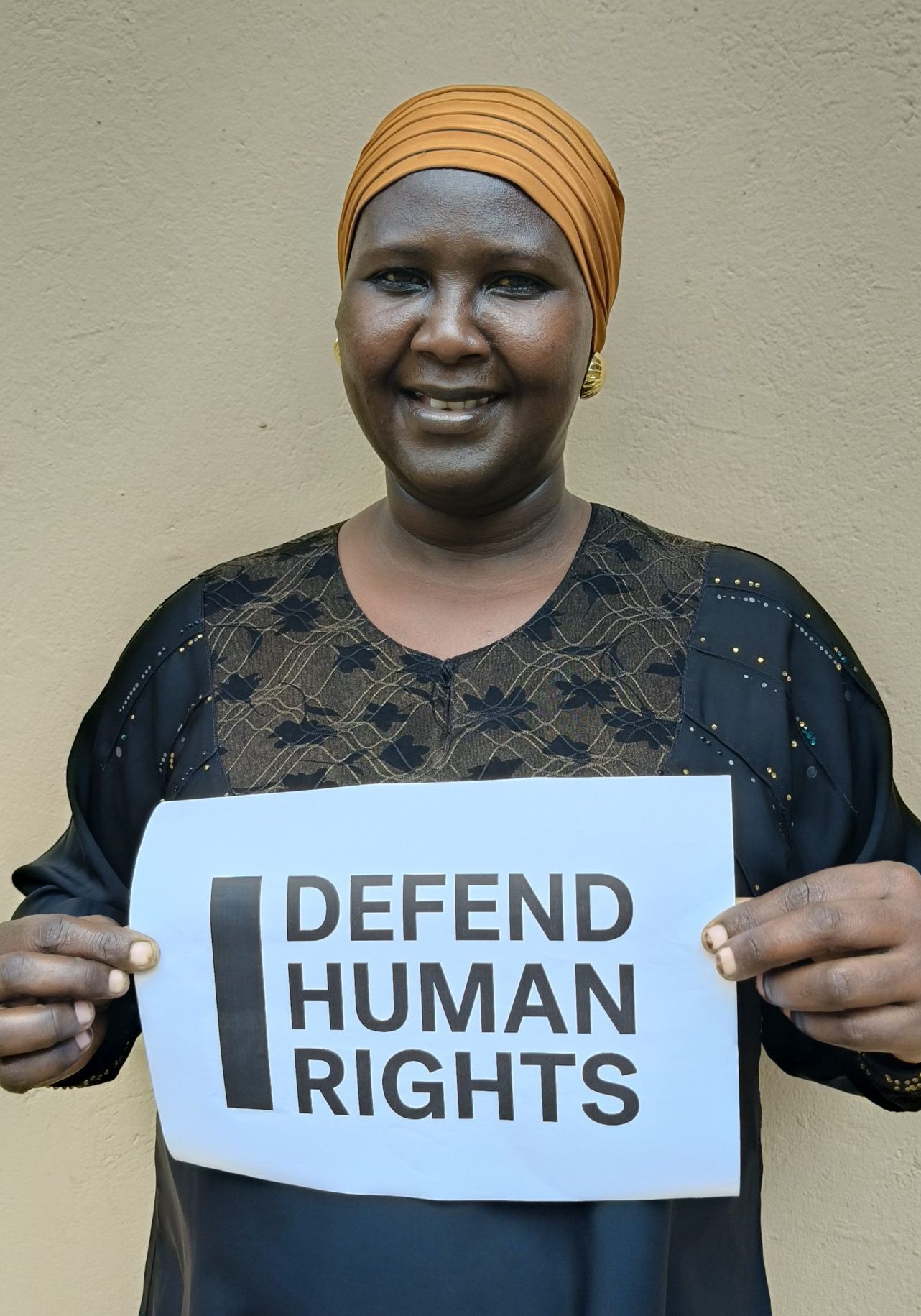 Margret Nabasirye's brave action. They are looking into the camera smiling and holding a sign that says "I Defend Human Rights."