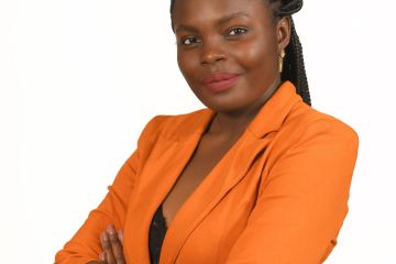 Picture of a dark-skin, young female with long black hair braided and tied back of the head. Wearing a orange blazer jacket and arms crossed across the chest. Looking directly to the camera with a slight smile.