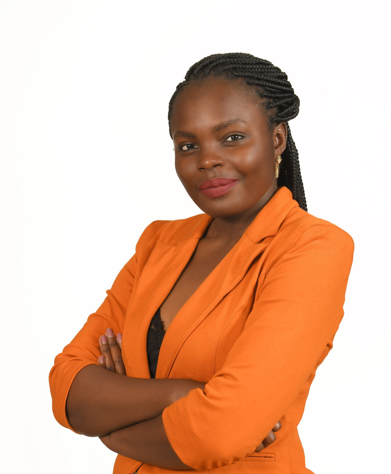 Picture of a dark-skin, young female with long black hair braided and tied back of the head. Wearing a orange blazer jacket and arms crossed across the chest. Looking directly to the camera with a slight smile.