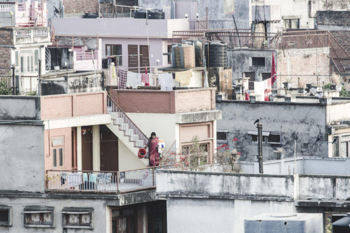 City view on roofs of houses. In the middle a woman walking down the stairs to a roof with laundry and a basket in her hands. .