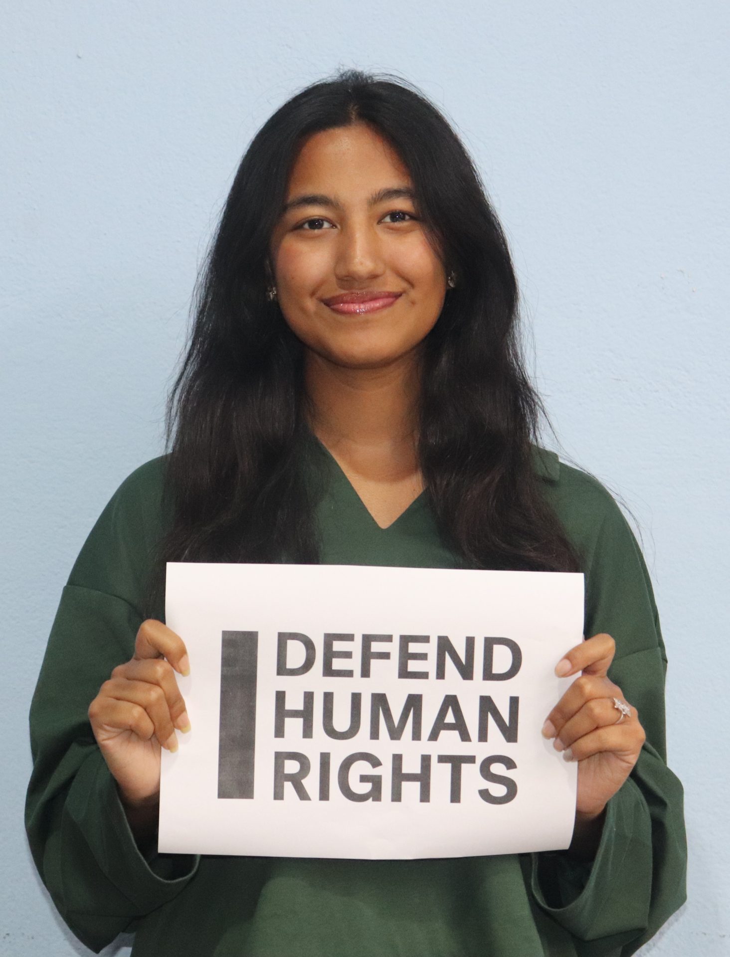 Jiya Rajbhandari's brave action. They are looking into the camera smiling and holding a sign that says "I Defend Human Rights."
